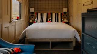 View of a bedroom with a double bed dressed in white linen and Peruvian woven cushions in black and white with red tassels.