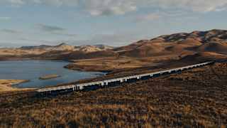The train travels through russet grasslands overlooking the curves and contours of Lake Lagunillas, seen from a hill above.