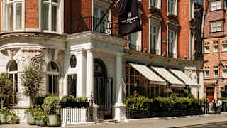 Corner view of The Cadogan Hotel where a branded black flag hangs above the portico entrance set into its Queen Anne façade.