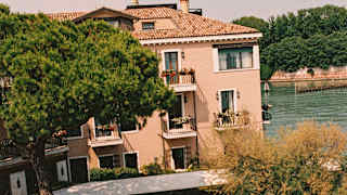 Two paved paths meet at a garden fountain, seen from above in a view that captures the hotel and the adjacent canal.