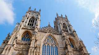 View from below of the ornate sandstone facade of York Minster under blue skies