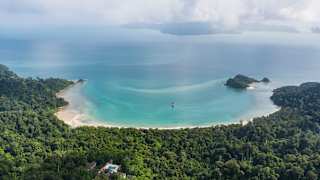 Areal view of Langkawi's Datai beach, sweeping between forested headlands, capturing a calm bay of dazzling blue waters.
