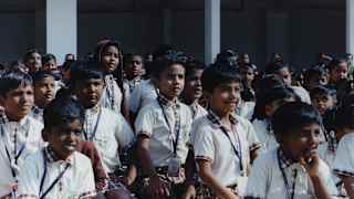 A group of school children with lanyards watch intensely as something happens off camera, in a close-up by Tara L. C. Sood.