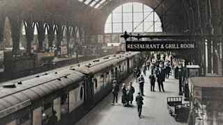 Historic photo of Kings Cross Station taken from above, capturing the Queen of Scots train, passengers and a restaurant sign.