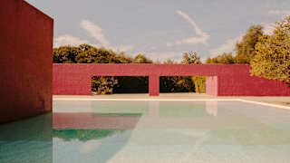 View over a shallow pool to a red wall with two flat arches belonging to the Cuadra San Cristóbal by architect Luis Barragán.