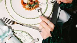 A guest wearing green satin enjoys a plate of smoked salmon with pretty garnish at a festive dining table, seen from above.