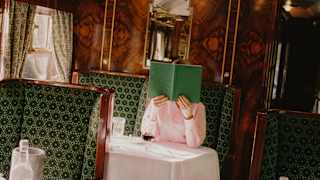 Angled image of a guest at a Cygnus carriage table as she holds a green menu, complementing the décor, in front of her face.