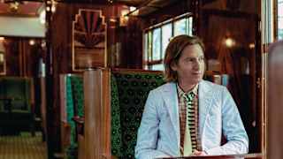 Filmmaker Wes Anderson sits at a French polished table in an art deco carriage and observes the world through the window
