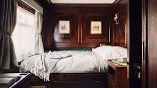 View through a Double Cabin to an unmade bed with white bedding, bathed in window light and encased in dark wood panelling.