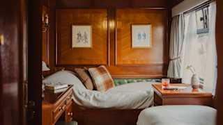 View of perpendicular single beds, seen through the doorway of a twin cabin filled with natural light from a window on the right.