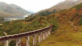 Aerial view of The Royal Scotsman as it crosses the Glenfinnan Viaduct on a damp and misty day, with views of Loch Shiel.