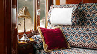 A large banquette in feather-pattern of blues and maroons and a plush red cushion catches light from the cabin window.
