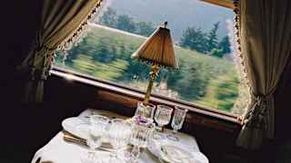 A green landscape rushes past a window framed by curtains next to an Etoile du Nord dining table, seen at an angle.