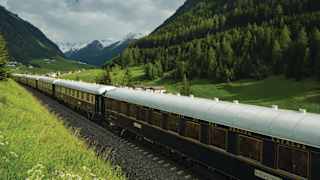 Gleaming blue train carriages with gold lettering in a verdant Alpine valley