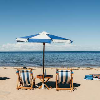 Two pairs of blue and white-striped deck chairs and matching parasols face Lake Titicaca on the cream sands of Collata Beach.