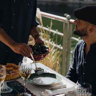 A crew member starts to ladle cooked mussels on to the plate of a male guest at a table set for lunch aboard Coquelicot.