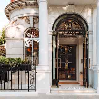 Beneath a white stone portico, The Cadogan Hotel's logoed wood and glass doors open to a glimpse of the gleaming interior.