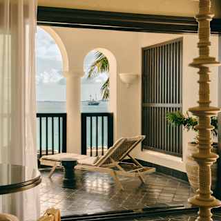 Bedroom view on to the balcony with smooth black Arabesque tiles and a sun lounger facing the wide ocean through open arches.