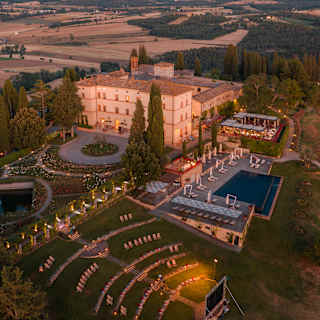 Magical aerial view of Castello di Casole at dusk, with the hotel, outdoor cinema and terrace illuminated with pretty lights.