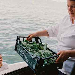 Chef Vania Ghedini lifts a crate of fresh greens through a hotel window, delivered by a boat visible on the canal below.