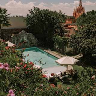 The still pool bathes in soft sunlight, seen over a bank of pink bougainvillea with the Parroquia's spires in the distance.