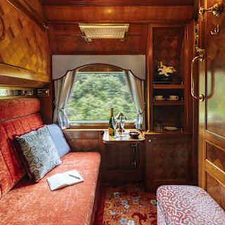 A book sits on the red banquette and a champagne bottle and two glasses wait on the window table in the cosy Pullman Cabin.