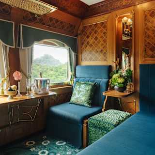 A velvet peacock-blue window seat soaks in views and luxury of the State Cabin, as champagne chills in a bucket on the table.