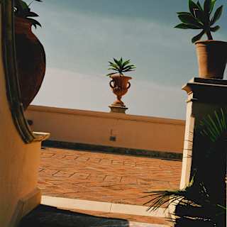 Detail of three ornamental urns containing succulents on the walls bordering a terracotta pathway, with a blue sky behind.