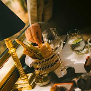 A diner's hand reaches for a seeded breadstick from a basket of rustic breads on a dining table with a wineglass and water.