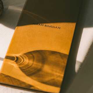 The refracted shadow of a wineglass creates pretty patterns on a closed, tan-covered Hiram Bingham-branded menu.