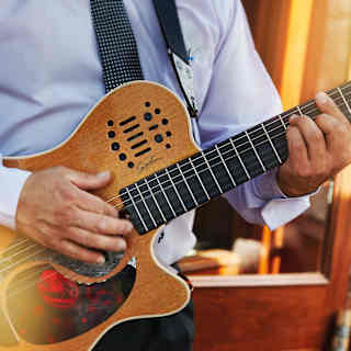 Close-up of hands plucking the strings of a wooden electric guitar