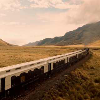 The Andean Explorer lets off steam as it heads through an Altiplano valley, with mountains either side, seen from just above.
