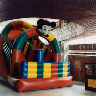 A red, blue, green and yellow inflatable slide with a Mickey Mouse-like figure fills a hall with an ornate carved mezzanine.