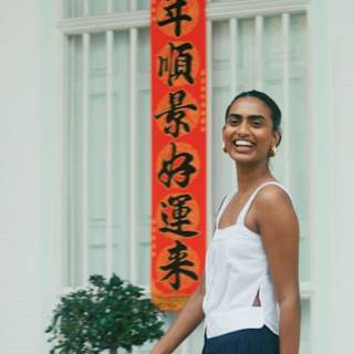 Kirthanaa Naidu, creative consultant, smiles to camera as she is photographed in a white top by an orange banner in Penang.