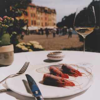 A knife and fork rest against a plate with three Santa Margherita prawns at a table with white wine set back from the marina.