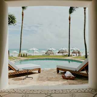 Four loungers surround a private pool set back from the sand, sea and beach parasols, seen from Villa Maroma's colonnade.