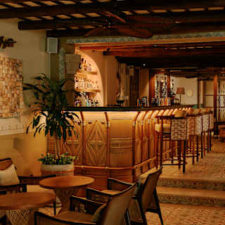 Pasta tiles flow from a seating area up two steps to a beautiful sub-lit bar, crafted with cane, with four wicker stools.