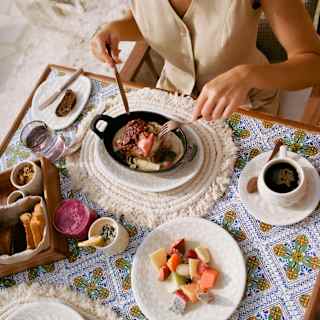 A guest of Casa Mayor tucks into Huevos Rancheros at a breakfast table with topped toast, coffee and a bowl of diced fruits.
