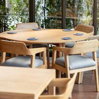 Looking over the pale wood dining tables and chairs to full length windows, offering a nature wall of forest views.