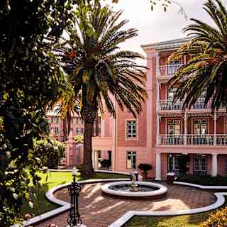 Hotel with pink walls and balconies overlooking palm trees and a fountain