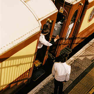 Looking down on a station platform where one British Pullman crew member talks to another who leans from a carriage door.