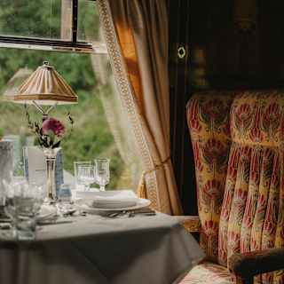 Soft window light falls on a dining table laid for guests and a padded, Art Deco beige and red chair, in a Gwen Car detail.
