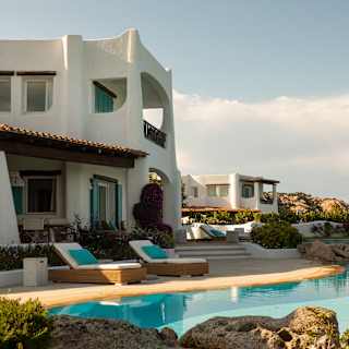 A five-bedroom villa with curved walls and white rendering overlooks a sunny pool, with another private villa in view behind.