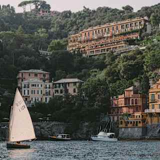 A single-sail boat drifts left of a view into Baia Cannone, overlooked by the magnificent Splendido hotel on a hill above.