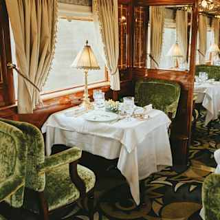 Luxury train dining car with garden-green velvet seating and crystalware on linen-coated tables