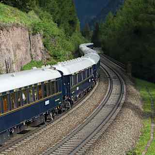 Gleaming blue and gold-detailed carriages snaking through a verdant valley