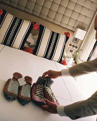 Tilted image of a staff member's hands as she lines four woollen heating pouches on a bed with a white, black and red pillow.