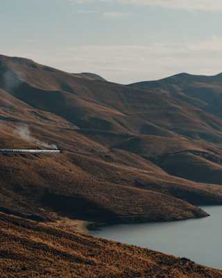 The Andean Explorer lets off steam as it cuts through the hill chain bordering Lake Lagunillas, grasses russet brown in sun.