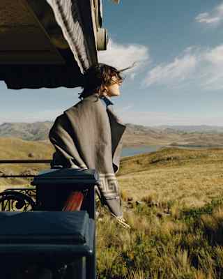 A dark-haired woman gazes at the grasslands over the rails of the Observation Deck, with the wind in her hair and shawl.