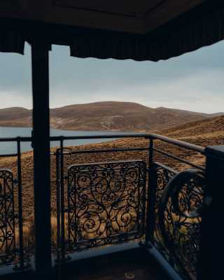 View from the corner of the Observation Car deck, through filigree iron railings to rolling brown hills bordering a lake.